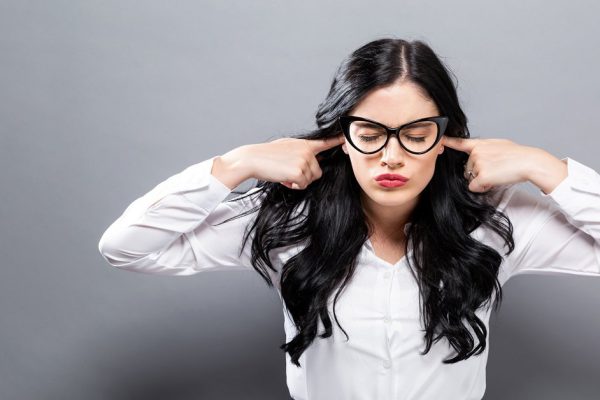 Young woman blocking her ears on a solid background