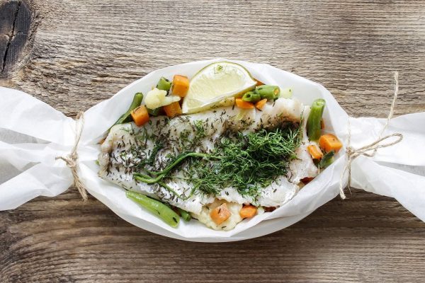 Fish in baking paper on rustic rough wooden table. Copy space.