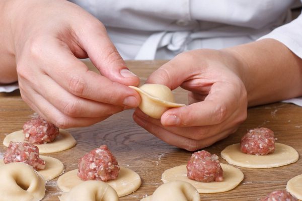 Cook hands sculpt dumplings with minced meat closeup