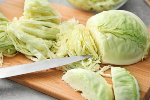Wooden board with cut cabbage on table
