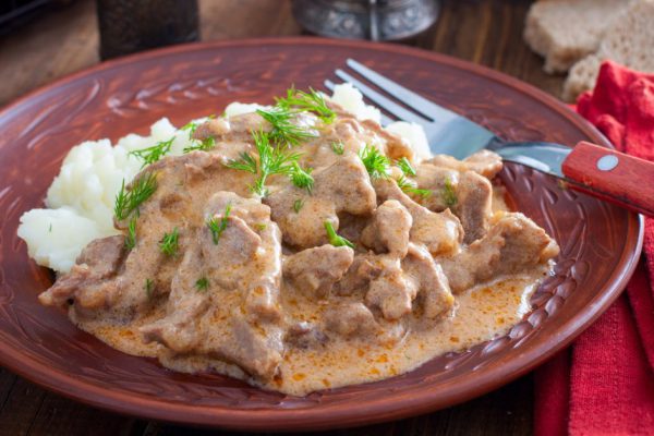 Traditional beef stroganoff in a ceramic bowl with mashed potato on a wooden table, selective focus