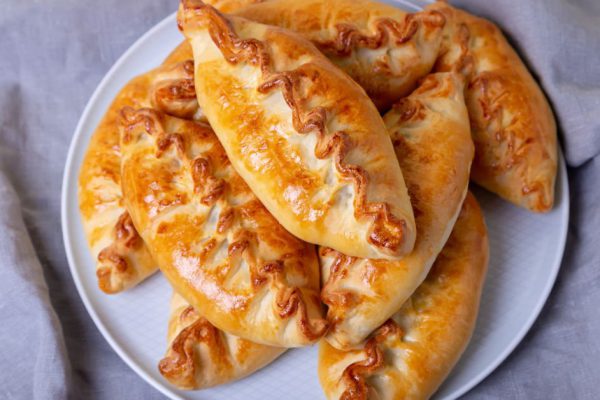 Pies (pirozhki) with cabbage. Homemade baking. Traditional Russian and Ukrainian cuisine. In the background is a dish with pies. Close-up.
