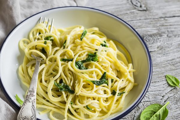 pasta with spinach and cream sauce on vintage enameled plate on a light wooden background