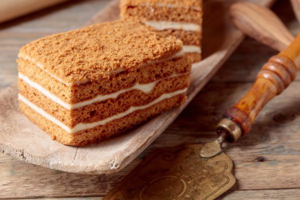 Layered honey cake with cream on a old wooden table.
