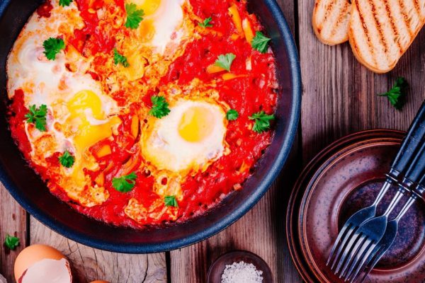 Shakshuka. Fried eggs with tomato, paprika and parsley on wooden table