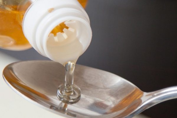 Housewife filling sunflower seed oil in a spoon, grey background