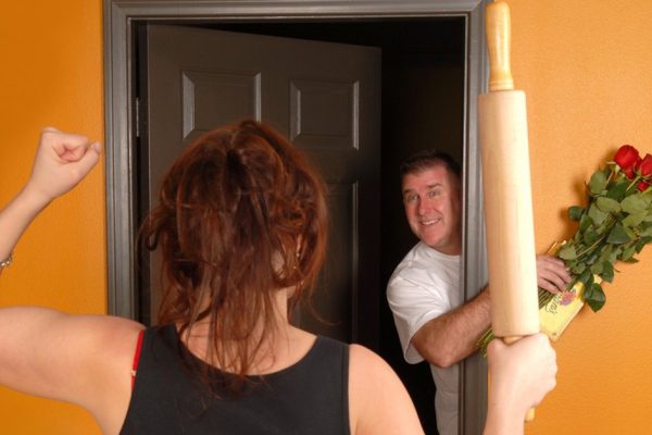 Husband coming home late to angry wife who is holding a rolling pin.