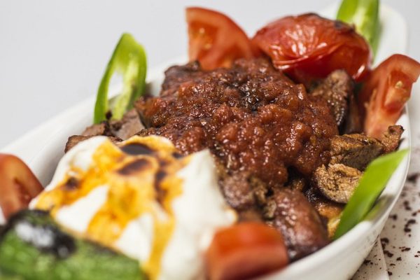 Traditional Turkish Bursa iskender kebap doner served with special red sauce and yogurt, garnished with grilled tomatoes and peppers