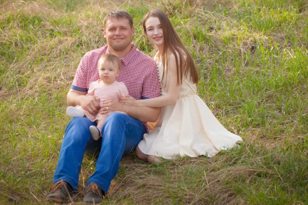The concept of a healthy family. Happy family on a walk. Mom, dad and little daughter are sitting on the grass.
