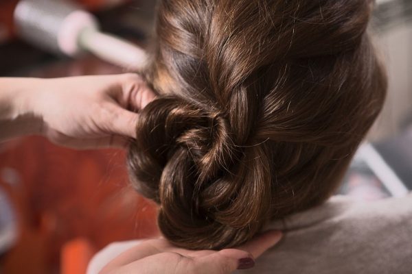 Closeup picture of beautiful lady sitting in chair and looking at mirror while hairdresser making braid in hairdressing saloon.