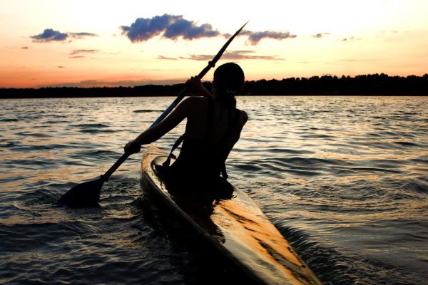 A female kayaker paddles across a lake against sunset