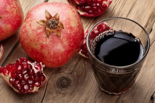 Glass of pomegranate juice with slices of pomegranate and whole pomegranate close up on wooden surface. Copy space. Top view.  Free space for text