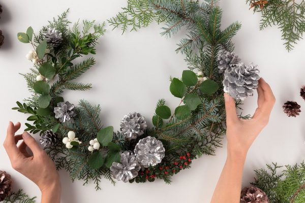 cropped view of hands making christmas wreath from fir branches, pine cones and mistletoe, isolated on white