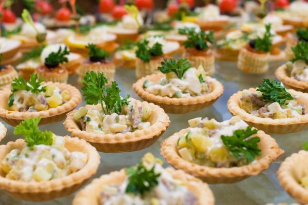 many tartlets with meat salad under mayonnaise and parsley on buffet table, shallow DOF