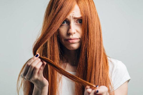 Hair care mistakes, bleaching problems concept. redhead woman holding her dry, damaged hair on white background