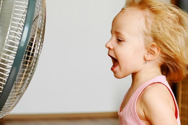 A little girl standing in front of fan