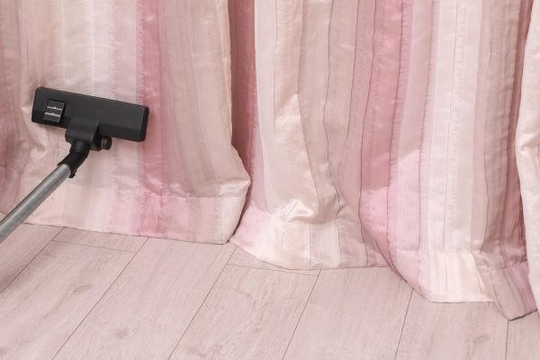 Removing dust from beautiful curtains with professional vacuum cleaner indoors