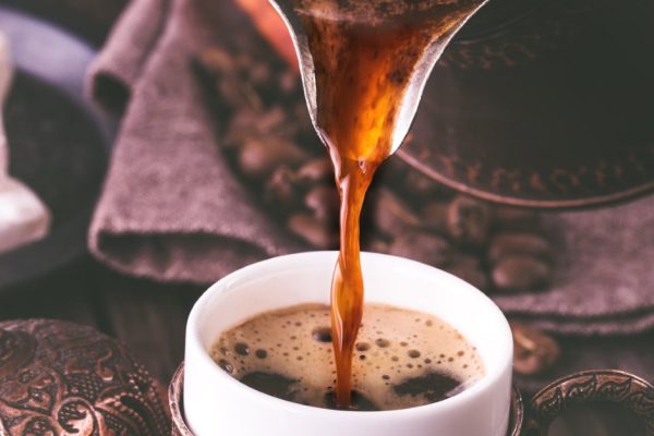 Pouring turkish coffee into traditional embossed metal cup.Toned