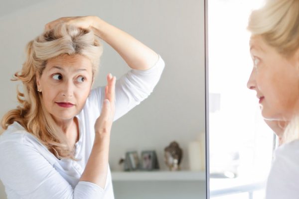 Senior beautiful woman checking her hair in front of mirror at home.