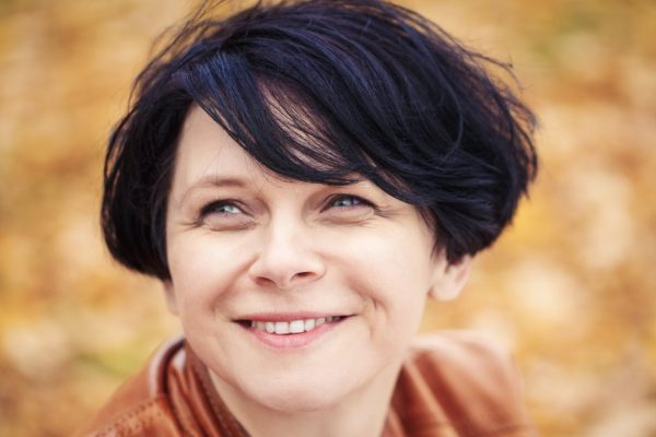 Closeup portrait of middle aged caucasian dark haired brunette woman with short bob hairstyle in light brown leather jacket  looking up smiling outside in autumn fall park