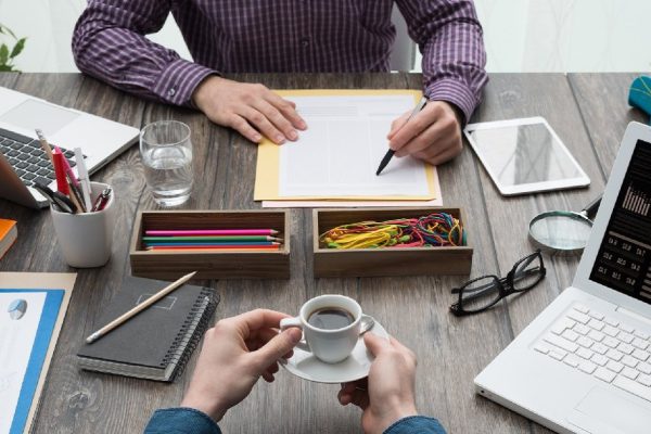 Businessmen working at office desk, they are checking paperwork and drinking a cup of coffee, point of view shot