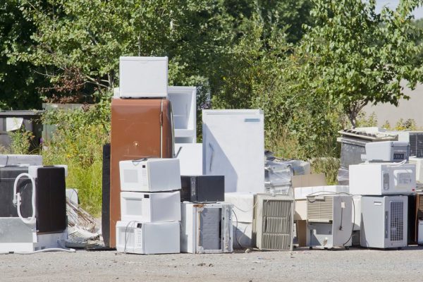 A stack of old appliances such as refrigerators, freezers, and air conditioners stacked up in a pile at a recycling garbage dump.