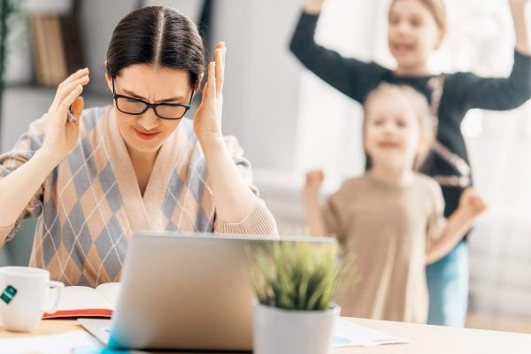 Woman working on a laptop. Noisy children and remote work from home.