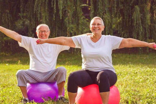 Senior exercise - Smiling pensioner couple doing fitness exercises on fitness ball in park