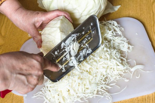woman shredding cabbage on cutting board on table
