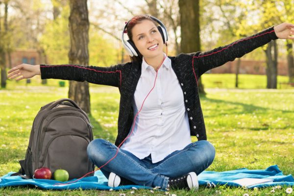 My song, my place and my freedom. Young girl in park with arms outstretched as if she's flying while listening music