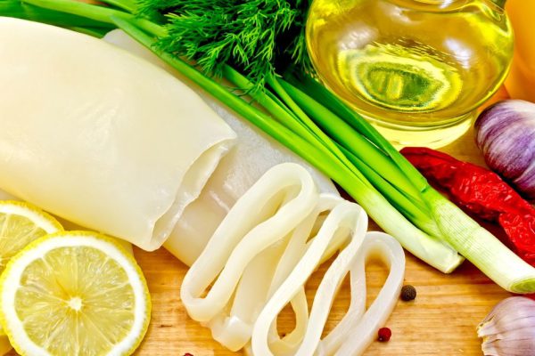 Squid whole and sliced ring, lemon, chives, dill, garlic, different peppers, a bottle of vegetable oil on a wooden board