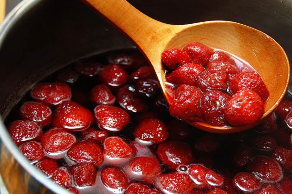 cooking strawberries preserves in metallic pot with wooden spoon