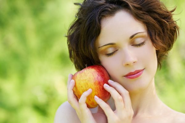outside portrait of beautiful young curly woman with eyes shut with red apple in park