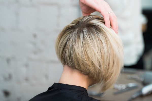 Closeup portrait teen young girl woman sitting in chair in hair salon looking in mirror while hairdresser checking her new haircut.