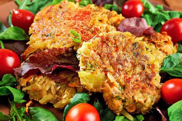 Homemade veg burgers from potatoes and lentils, served on a plate with tomatoes and green salad on a wooden background; close up.