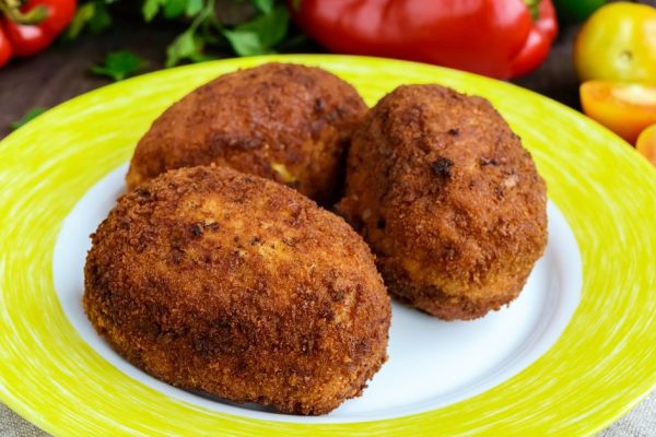 Meat mini-rolls (cutlet) with boiled egg in a clay bowl on dark wooden background.