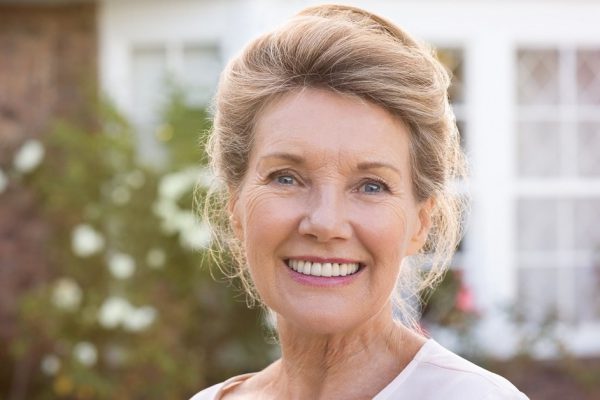 Happy senior woman standing outside her house. Content woman smiling and looking at camera. Portrait of cheerful old grandmother relaxing outside the house.