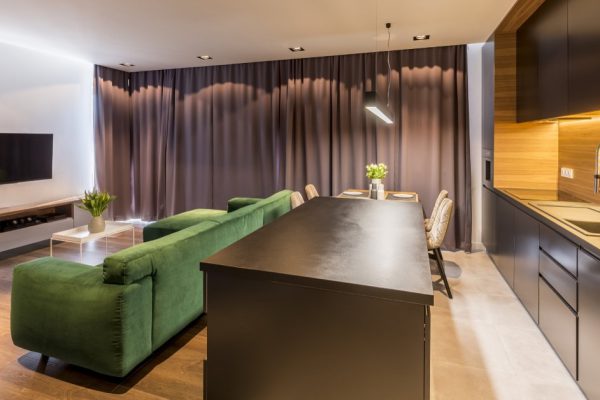 Kitchen island and green couch in dark open space interior with grey drapes and television