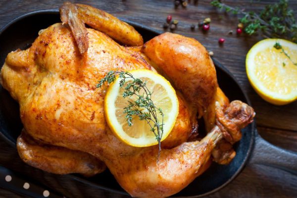 Whole roasted chicken with lemon and thyme on a pan. Rustic style.