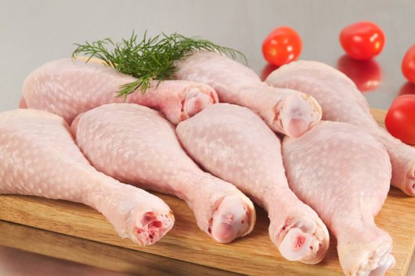 Fresh raw chicken legs arrangement on kitchen cutting board with tomatoes