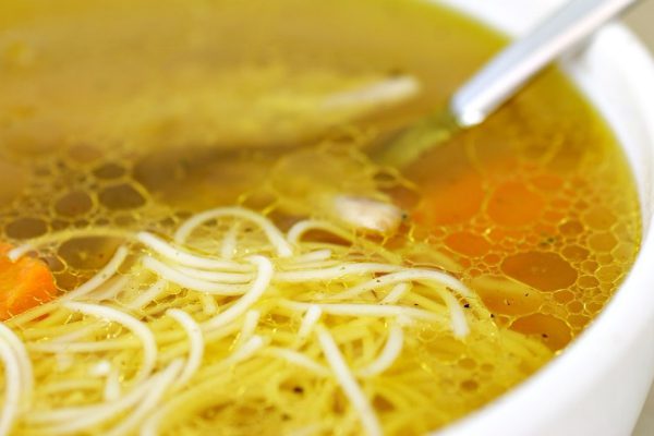Chicken soup with noodles in white plate with spoon.