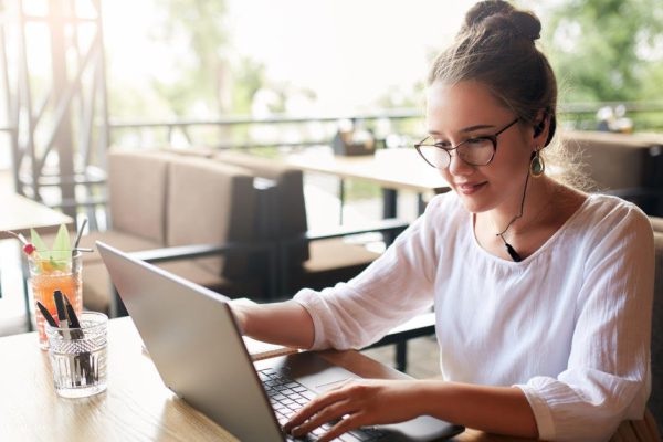 Businesswoman working remotely at cafe with headset and laptop. Mixed race female performing business negotiations on conference video chat. Telecommuting concept. Freelancer speaking on cellphone via headset.