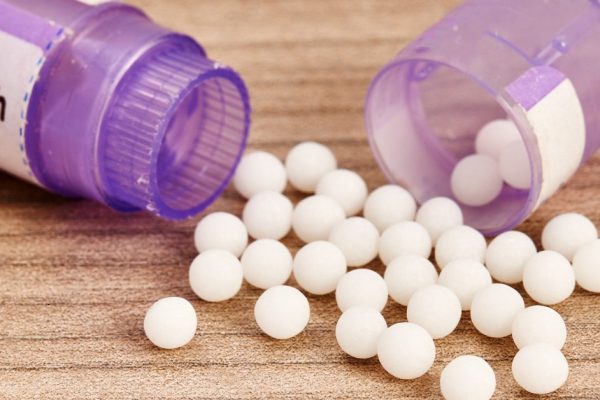 Homeopathic granules scattered on a wooden table close to their purple containers