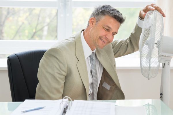 Portrait Of A Happy Businessman Sitting Near Fan In Office
