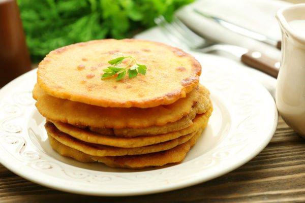 Stack of corn tortillas with stuffing and greens on wooden table background