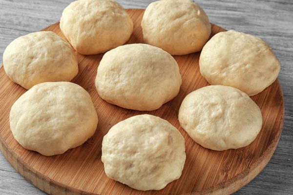 Wooden board with balls of raw dough on kitchen table