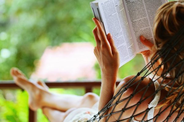 Young woman reading a book lying in a hammock