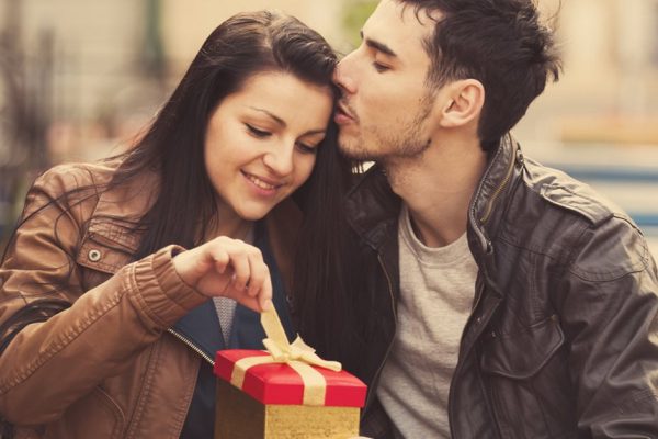 The young man gives a gift to a young girl in the cafe and they are kissing.