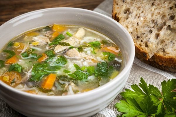 Chicken rice soup with vegetables in bowl and bread on rustic table