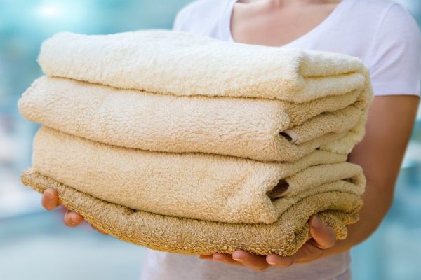 Woman holding clean towels on blurred background.